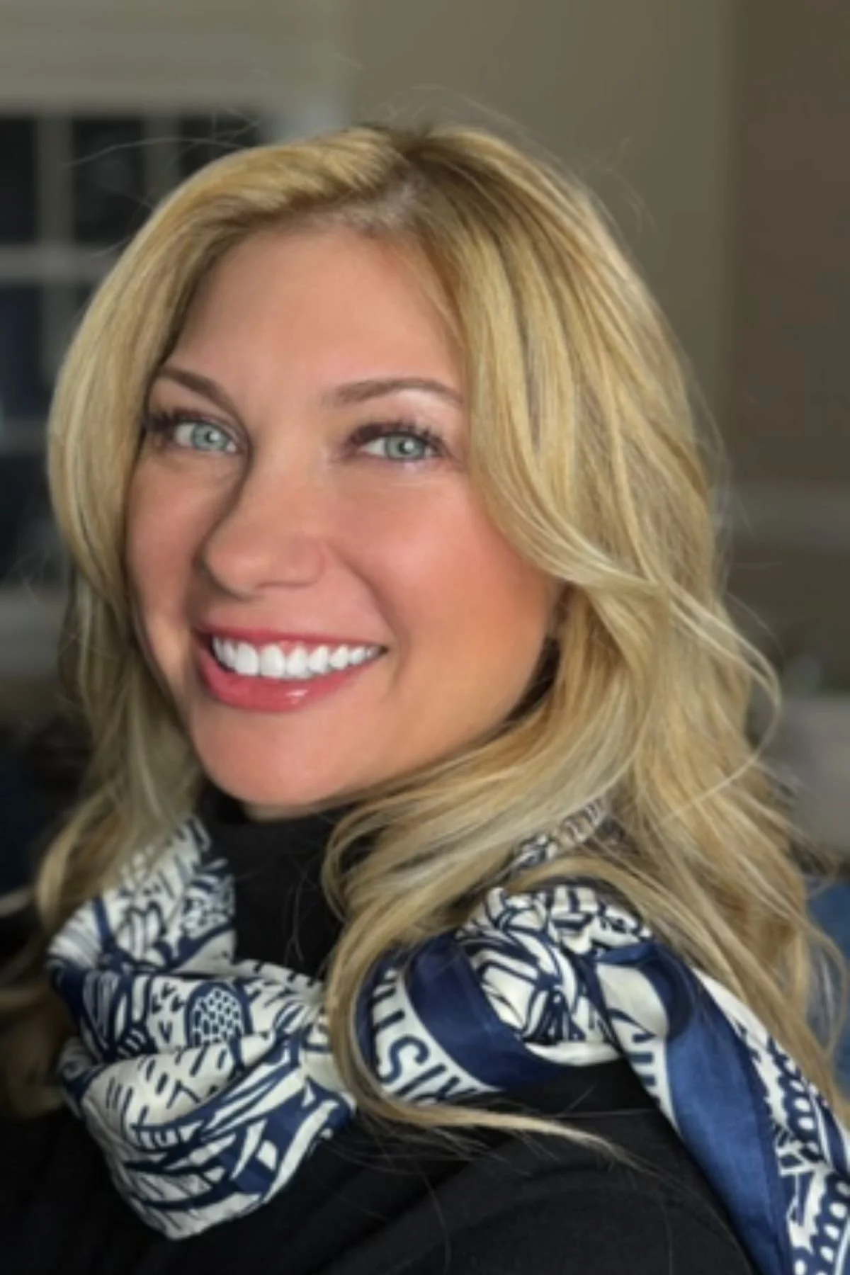 A smiling woman with blonde hair and blue eyes, wearing a patterned scarf.