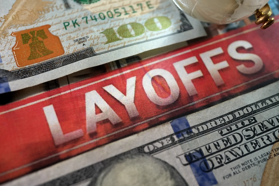 Close-up of US currency including a $100 bill and a pink and black Layoff Offs banner.