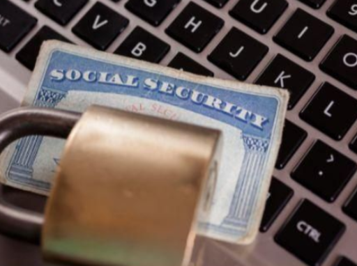A Social Security card with a padlock on top, resting on a laptop keyboard.