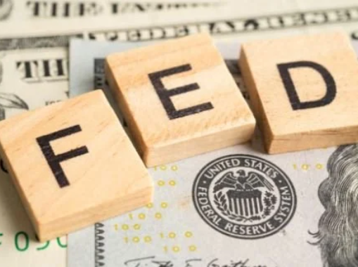 Three wooden Scrabble tiles spell out 'FED' placed on top of U.S. dollar bills.