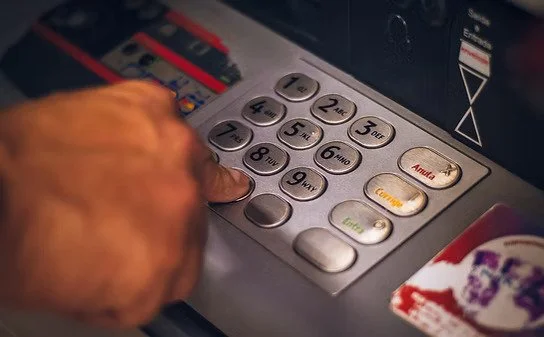 Close-up of a person's hand pressing buttons on an ATM or bank card reader machine.
