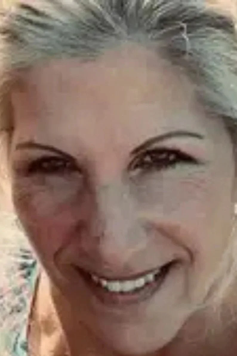Close-up of a woman smiling with gray hair and wearing makeup.