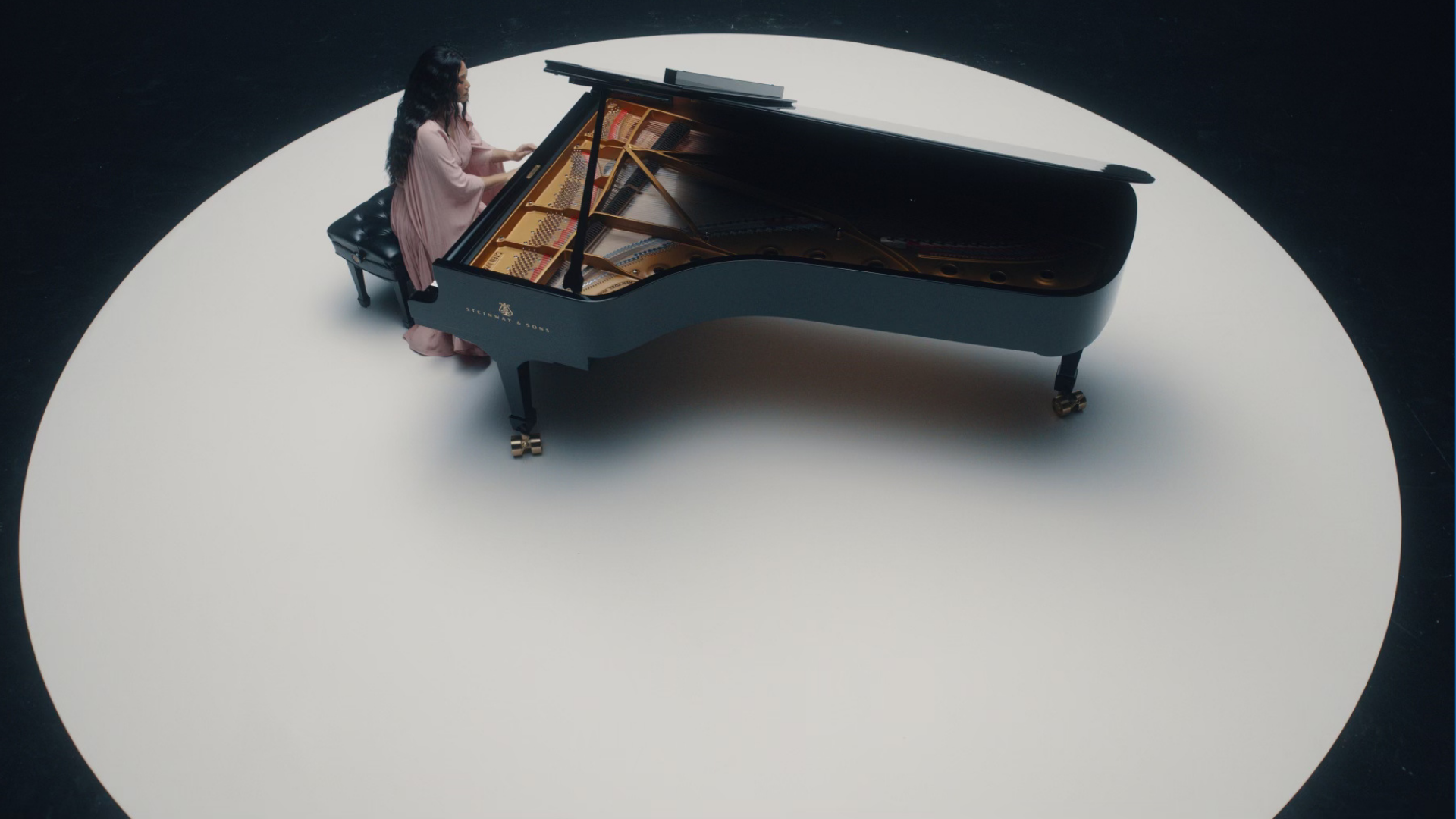 Scene from a commercial production delivered by The Aux Co featuring a woman in a pink dress playing a grand piano on a circular white stage