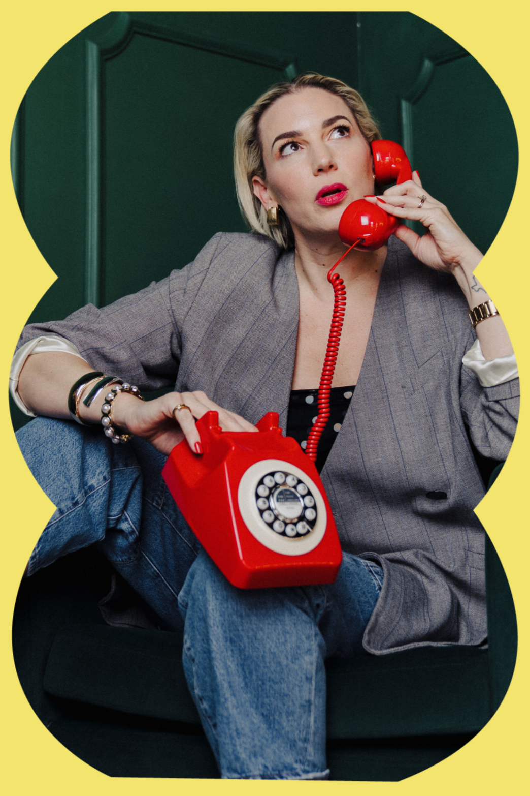 Dani Dufresne, founder of The Aux Co, holding a red rotary phone while sitting on a chair, representing her bold and hands on approach to creative production leadership.