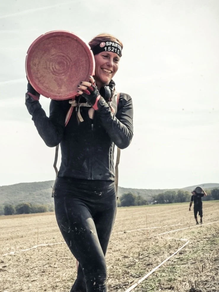 A woman in athletic gear holding a pink frisbee, smiling, outdoors in a field with another person in the background.