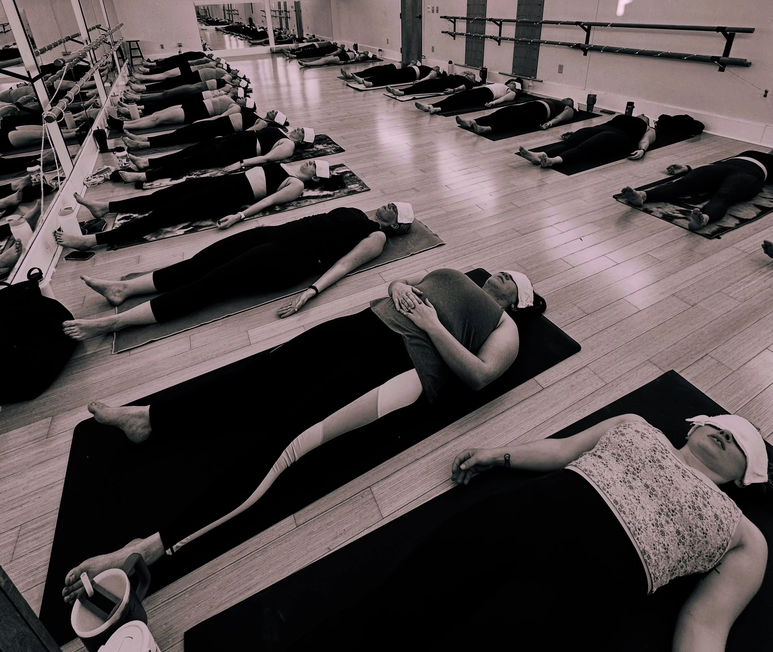 People participating in a yoga or meditation class lying on mats with eyes covered, in a calm indoor studio.