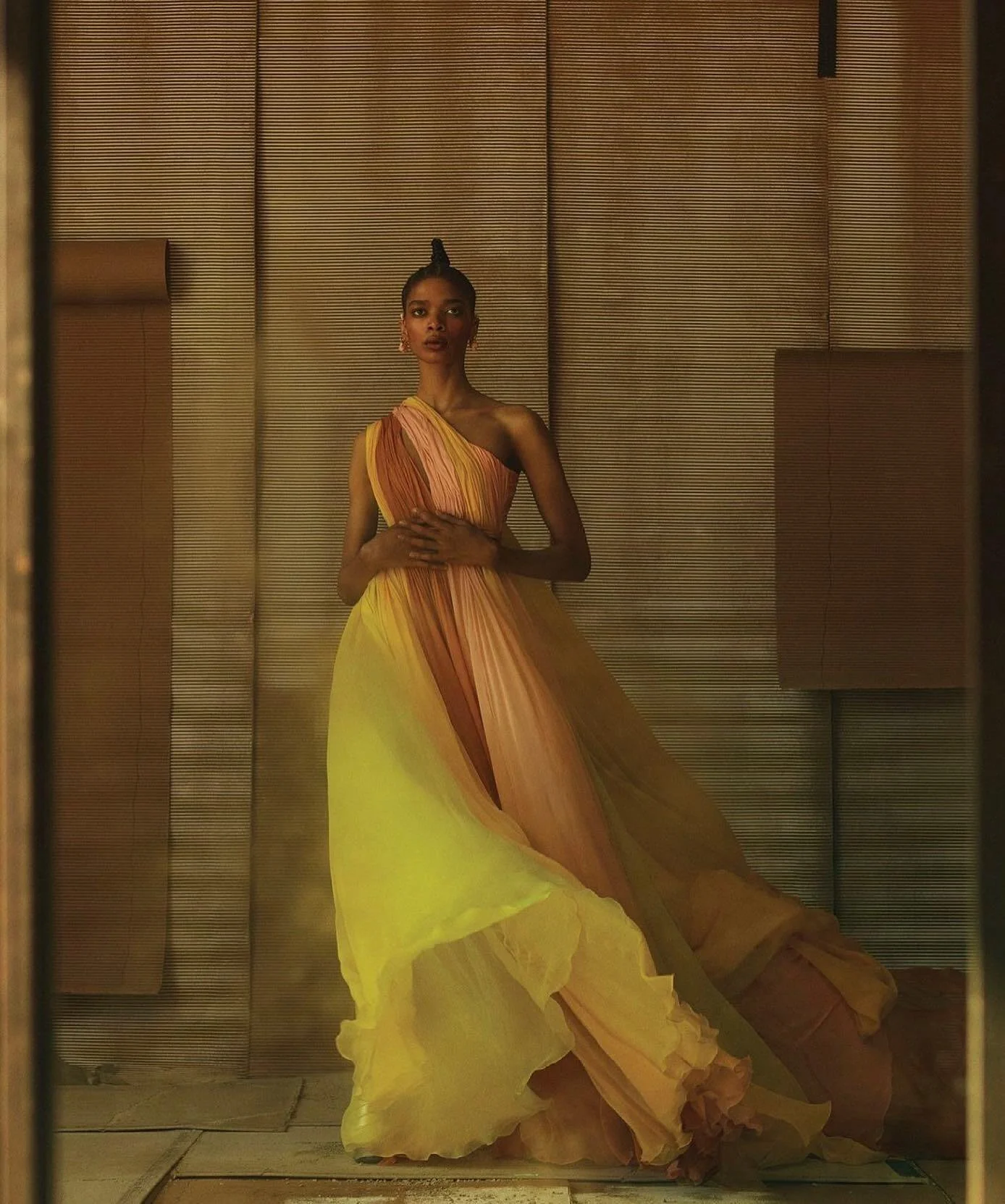 A woman in a flowing, multicolored gown standing in front of a textured wall.