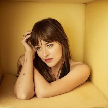 Woman with brown hair and bangs, resting her head on her hand in a yellow box-shaped room.