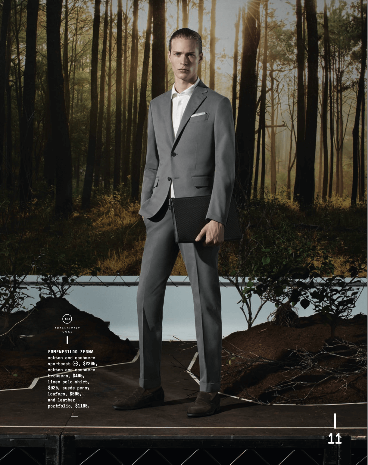 Man in gray suit with white shirt holding a black portfolio, standing on a stage with a forest background.