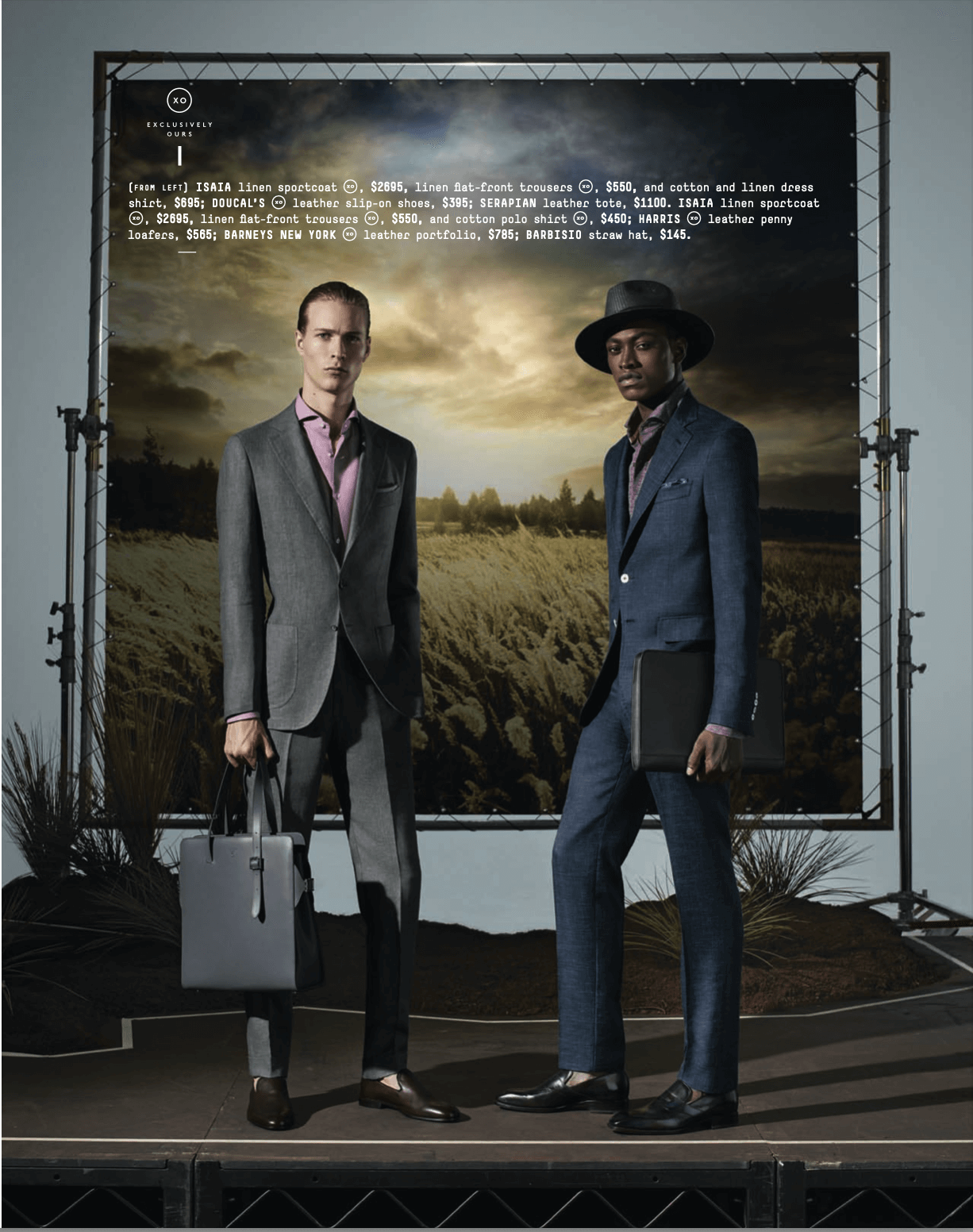 Two men in suits standing in front of a backdrop resembling a countryside landscape with a sunset sky, one holding a briefcase and the other a laptop case.