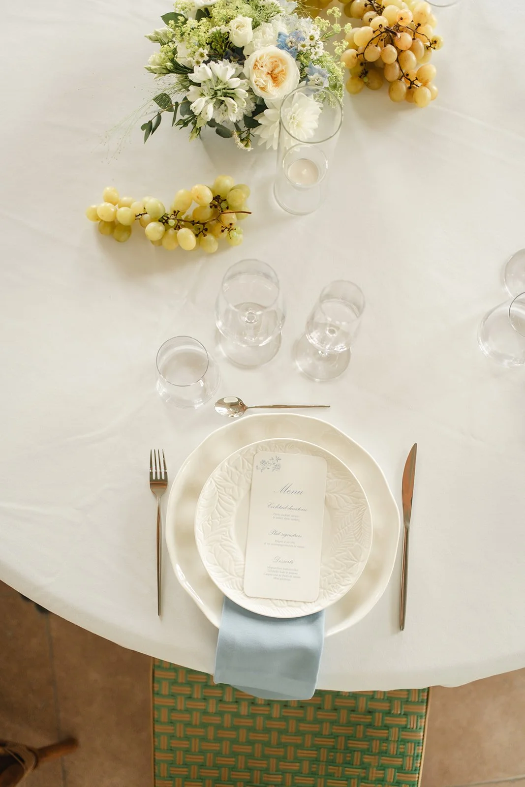 Table élégante avec une assiette, un menu, une fourchette, un couteau, un verre, un vase avec des fleurs et des grappes de raisin.