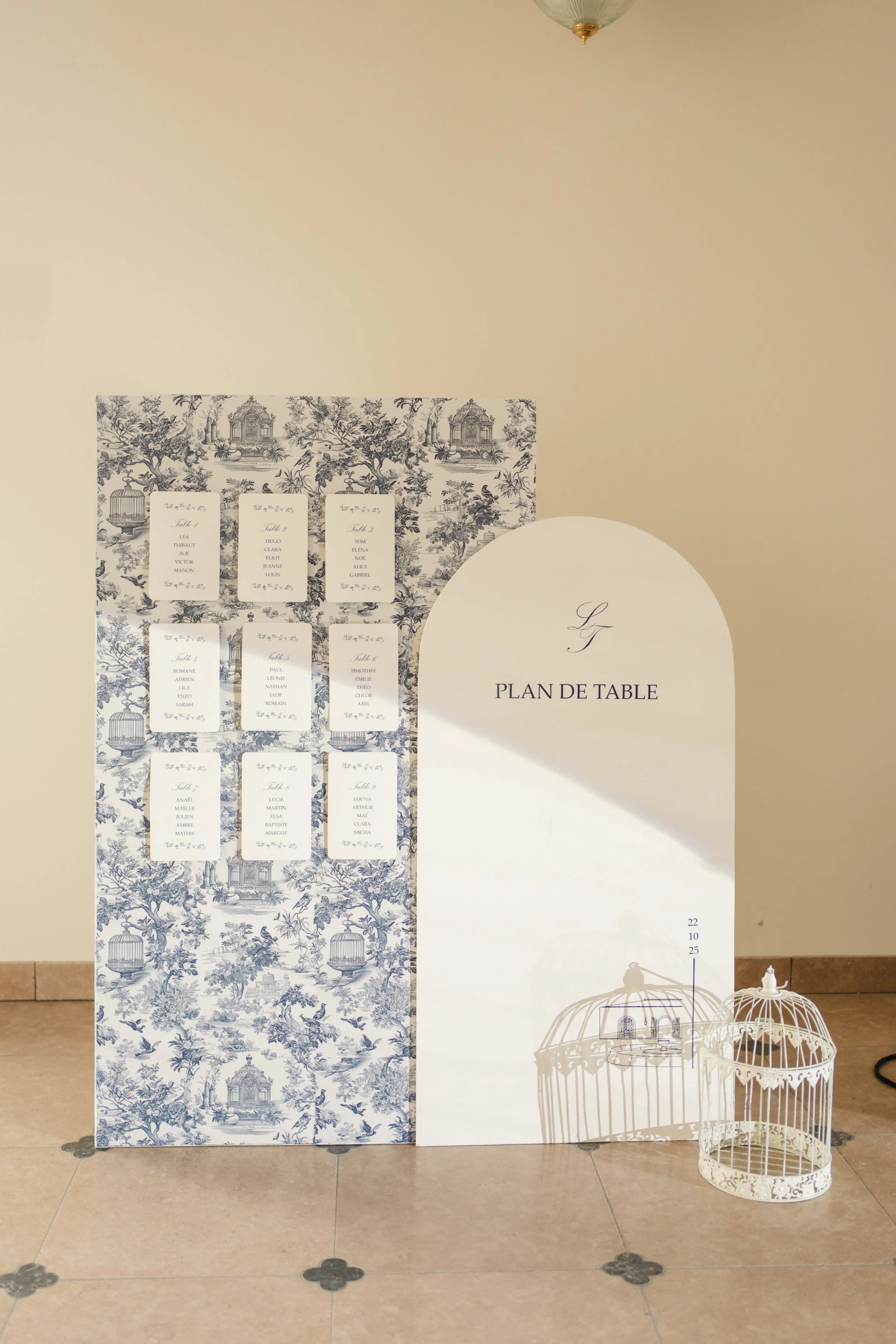 Plan de table pour un événement, avec plusieurs papeterie pour différentes tables, décor de toile avec motifs de jardins et oiseaux, et une cage à oiseaux blanche en métal.