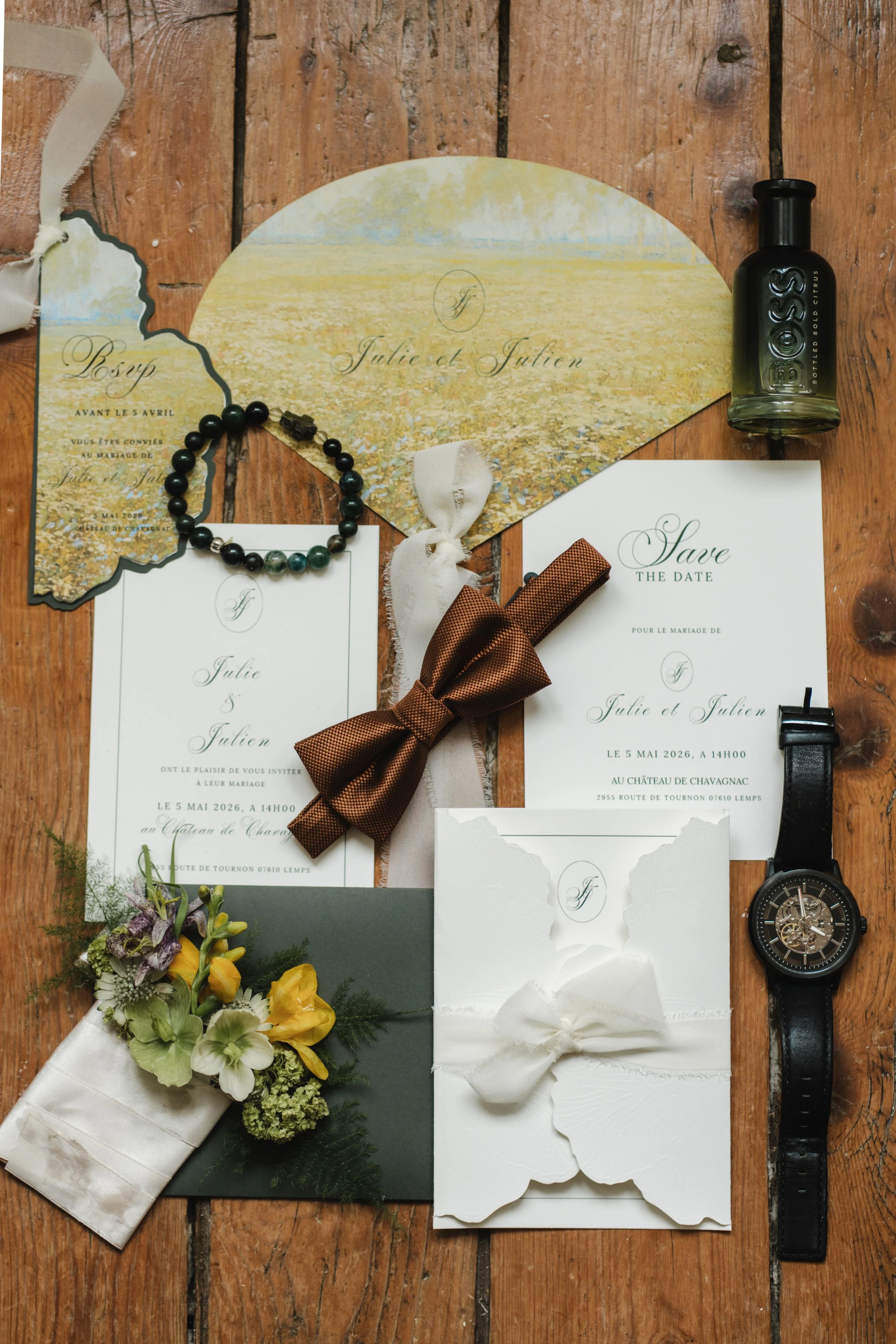 Collection d'objets liés à un mariage, y compris des invitations, un bracelet en perles, un ruban marron, une bouteille de parfum, une montre-bracelet, et un bouquet de fleurs. La surface est en bois.