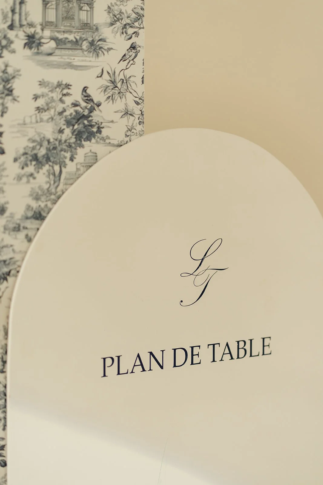 Plan de table pour un événement, avec un fond beige et une partie de papier à motif noir et blanc représentant une scène bucolique avec des oiseaux.