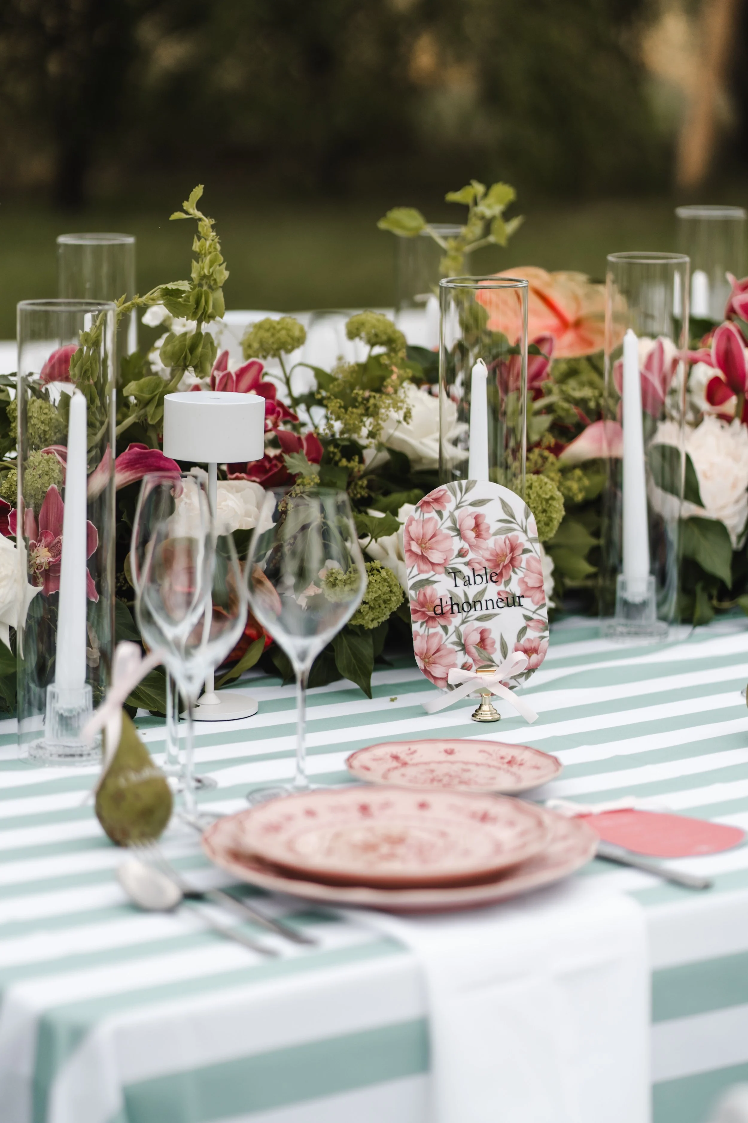 Table de mariage en plein air avec décor floral, bougies, vaisselle en porcelaine, et une carte nommée "Table d'honneur".