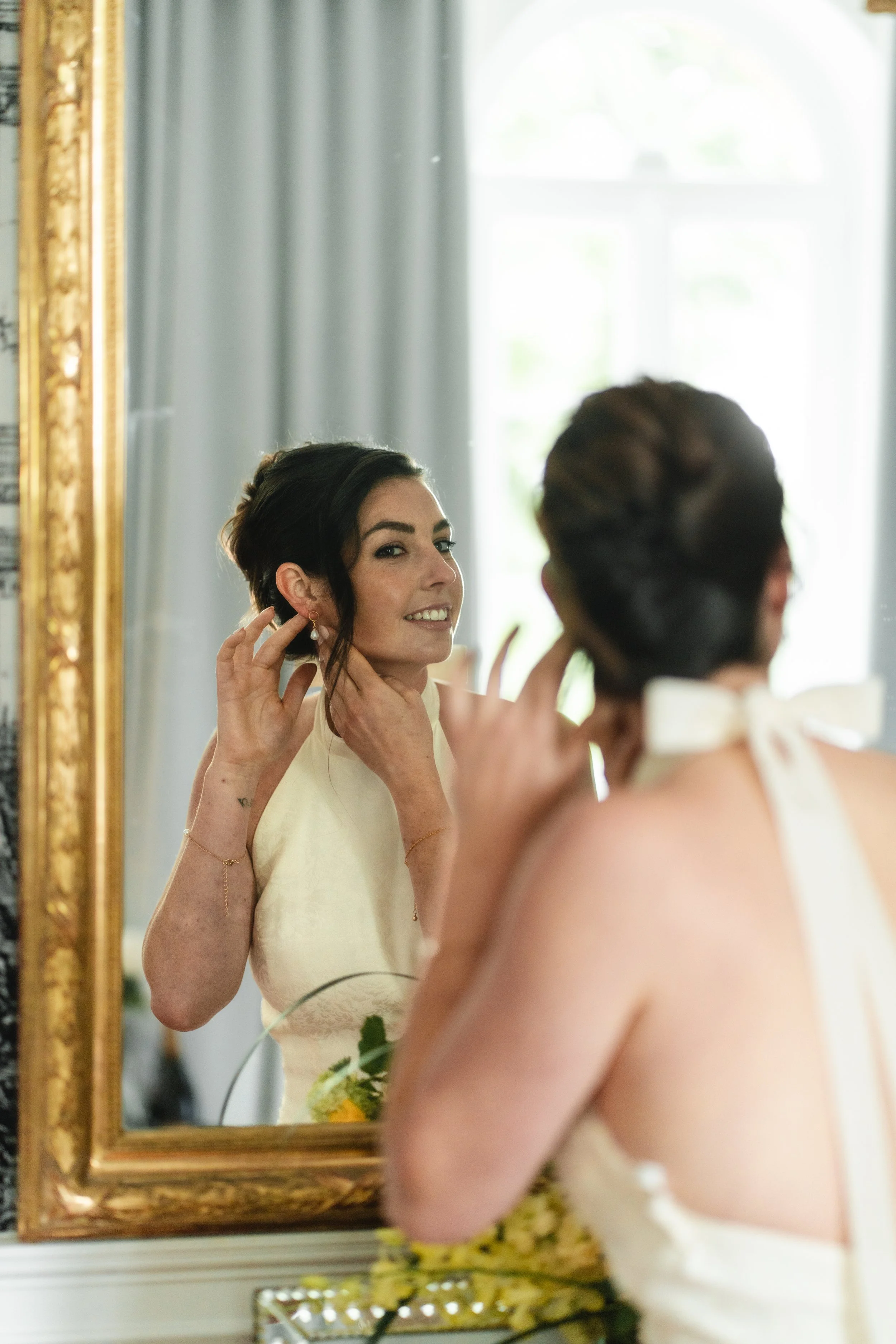 Une femme élégante s'apprête à mettre un boucles d'oreilles en regardant dans un miroir doré.