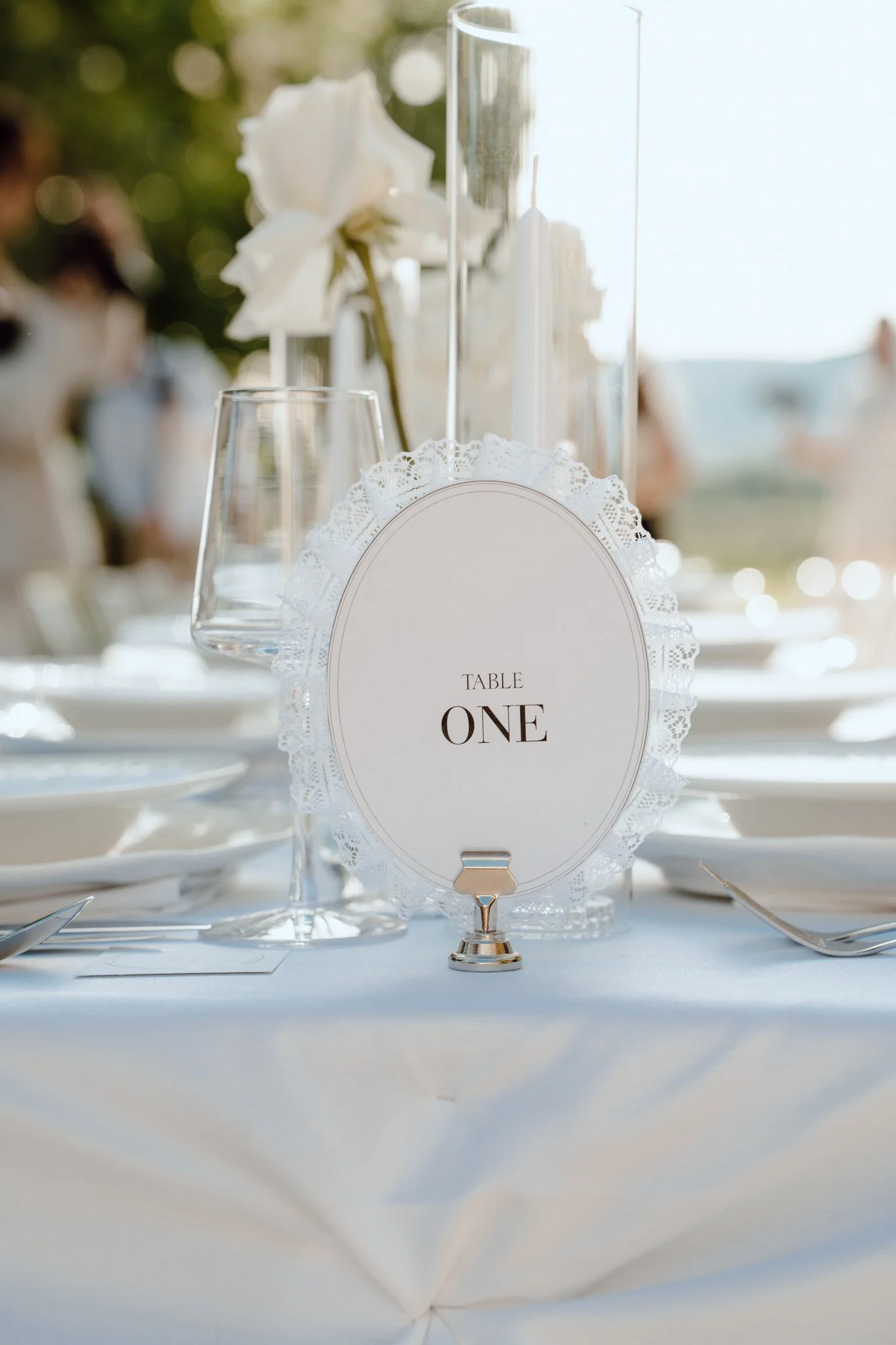 Table de mariage élégante avec un centre de table floral, une carte de place indiquant la table numéro un, et des verres à vin blancs, dans un décor en plein air lors d'une cérémonie
