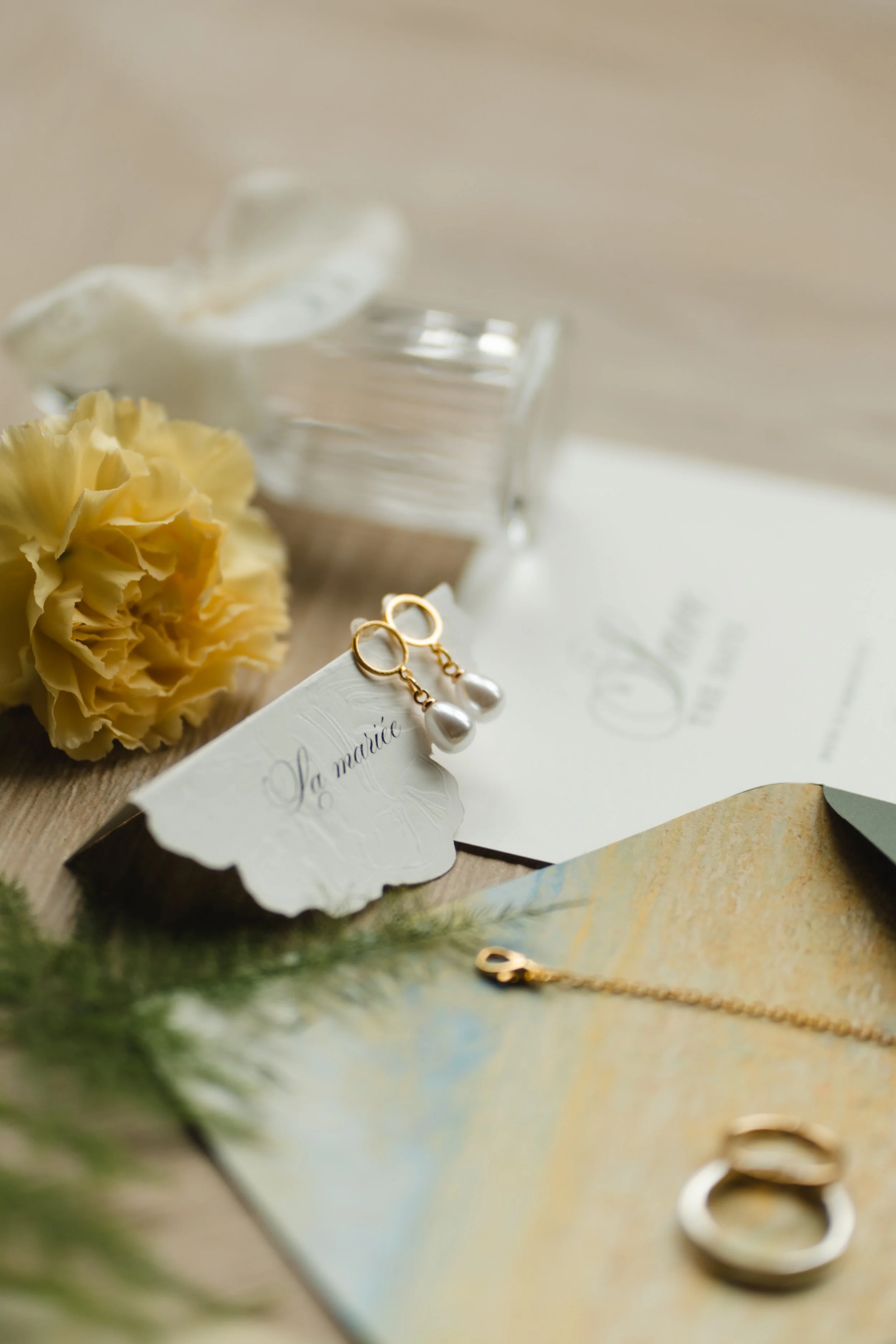 Bouquet de fleurs jaunes, boutons d'oreilles en perles et bracelets en or, fond beige.