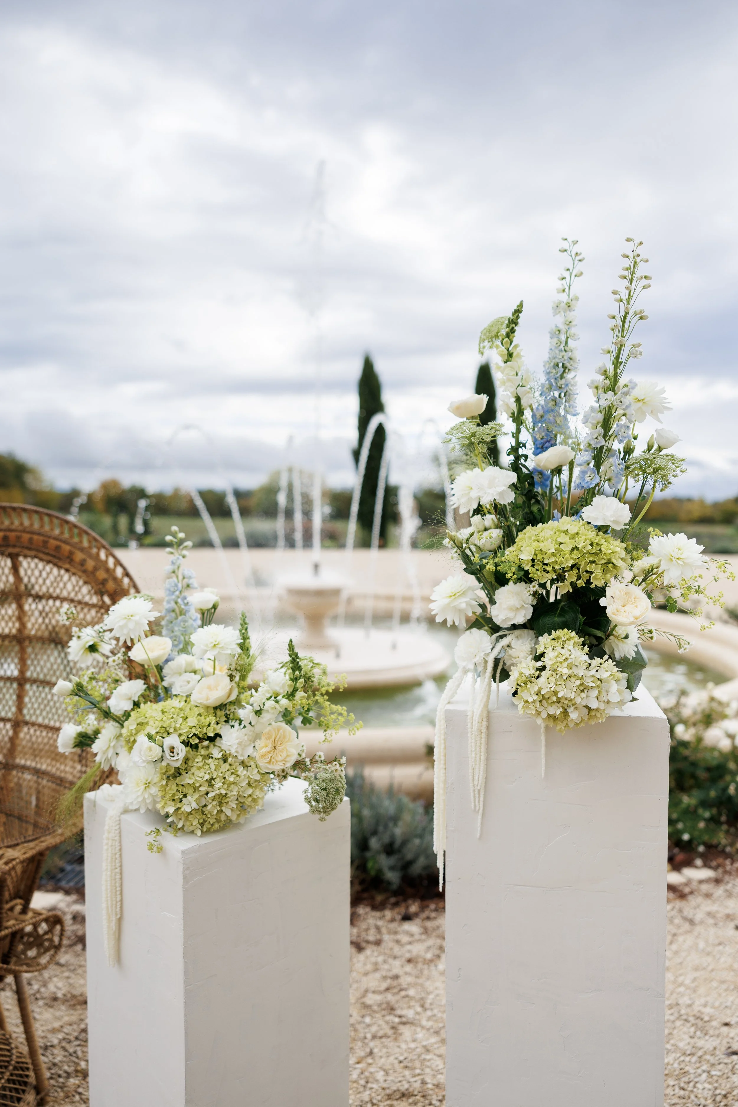 Arrangements floraux blancs et verts lors d'une cérémonie en plein air avec fontaine en arrière-plan.