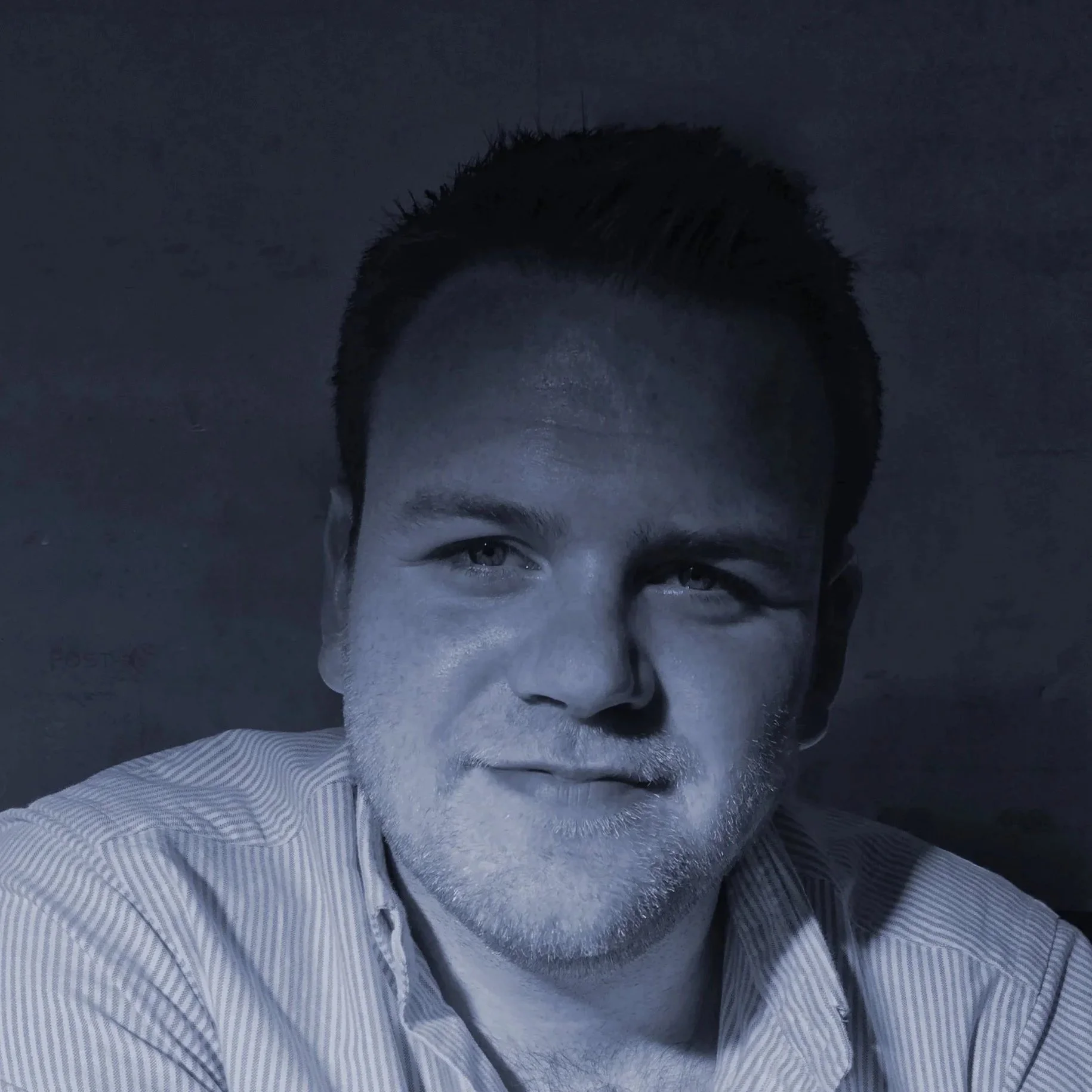Black and white portrait of a man with short dark hair and a light beard, wearing a striped shirt, looking slightly to the right with a mild smile, against a plain background.