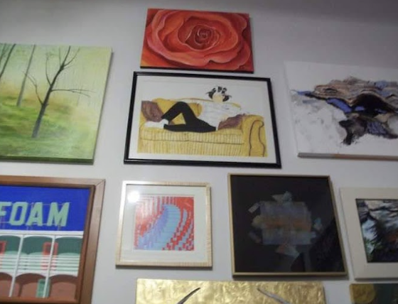A wall decorated with various framed paintings, including a woman lying on a yellow sofa, an abstract red rose, and several landscapes.
