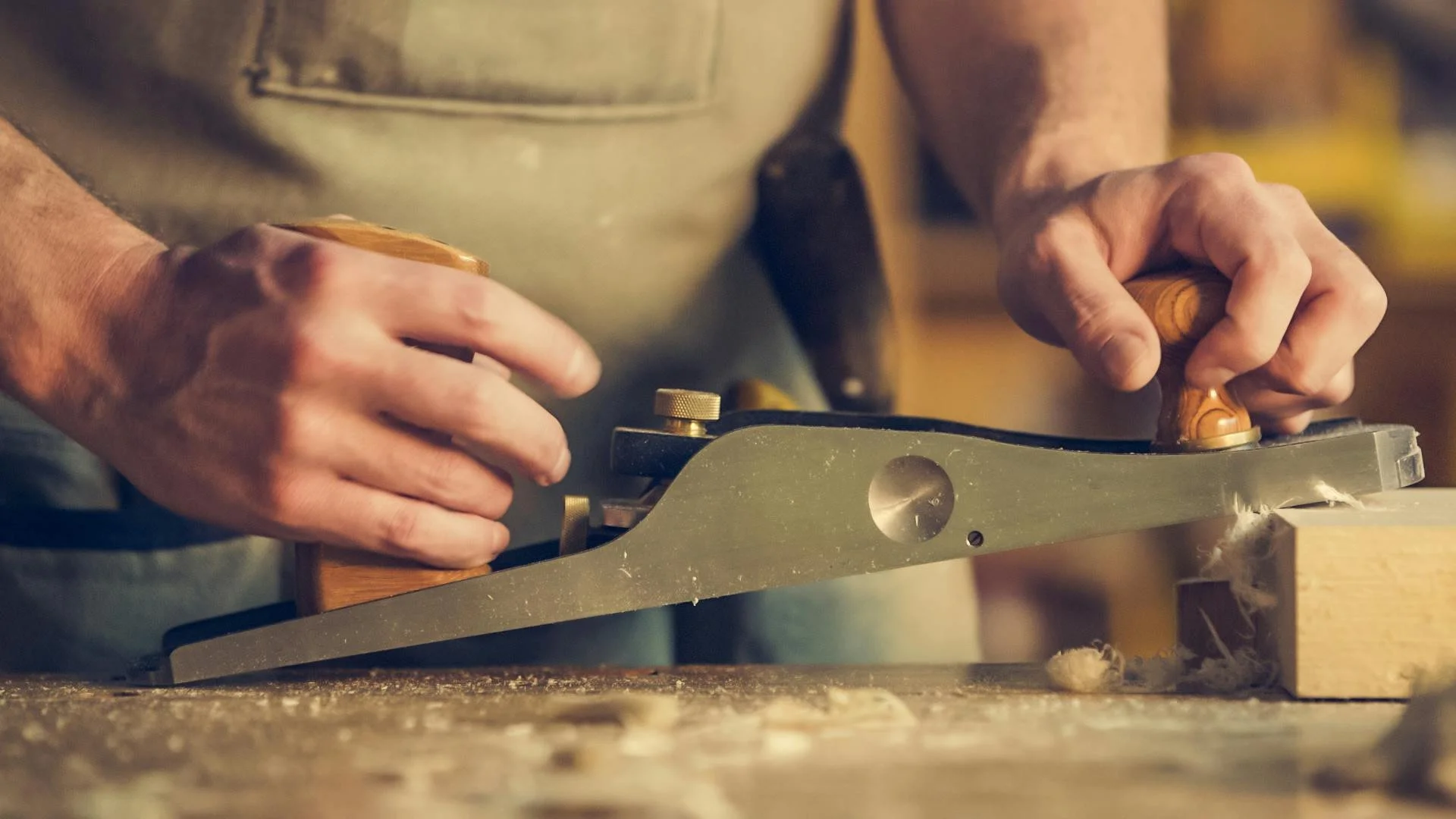 A person using a hand plane to smooth a piece of wood in a woodworking shop.