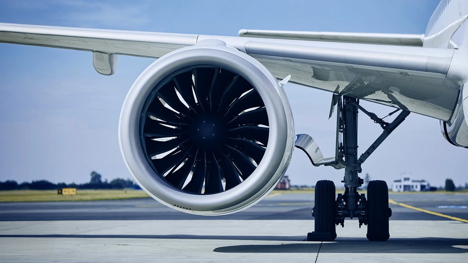 Close-up view of a modern jet airplane's engine and landing gear on the runway during daytime.