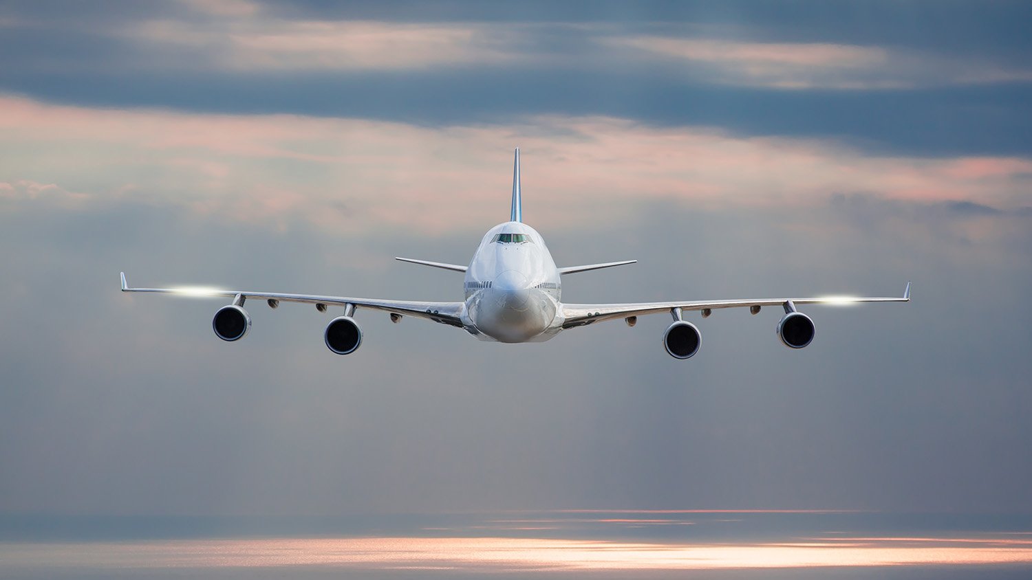 Front view of a commercial airplane flying in the sky during sunset.