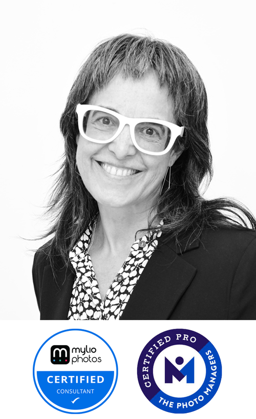 Black and white portrait of a smiling woman with shoulder-length hair wearing white glasses, a patterned shirt, and a dark blazer, with two certification badges at the bottom.