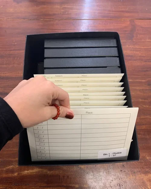 A hand holding a blank note card with columns for 'Subject' and 'Place' over a tray of similar cards, on a wooden surface.