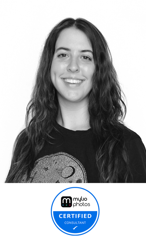 Black and white portrait of a young woman with long wavy hair, smiling, wearing a t-shirt with a moon and star design, and a 'Certified Consultant' badge on the bottom.