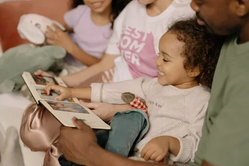 A man showing a photo album to smiling children, one girl reaching out to turn a page.