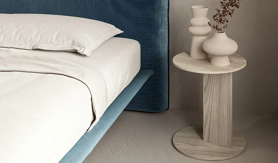 Cinquepuntozero Atlas Italian light wood round side table beside blue bed, modern design at ArkNova Interiors Paphos showroom in Cyprus