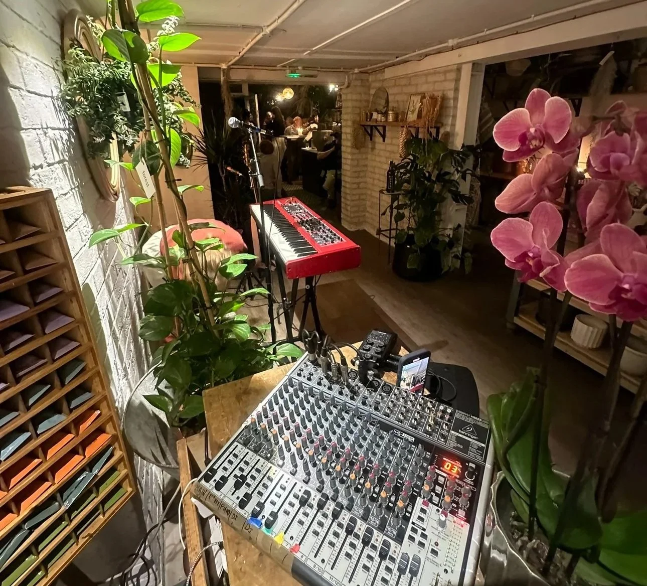 Picture of a plant shop with a mixing desk and electric keyboard in the center, surrounded by pink flowers and green plants