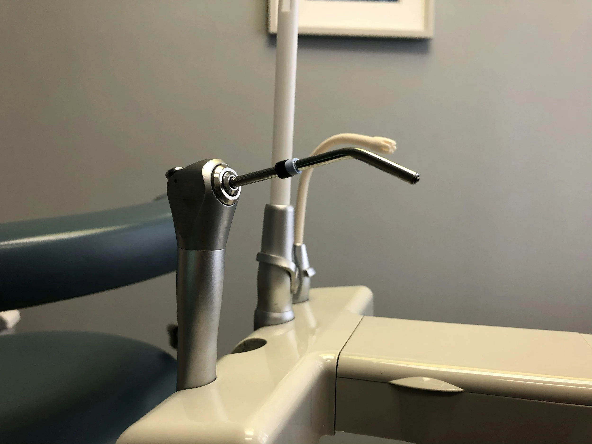 Dental chair with attached dental instrument and sink in a clinical setting.