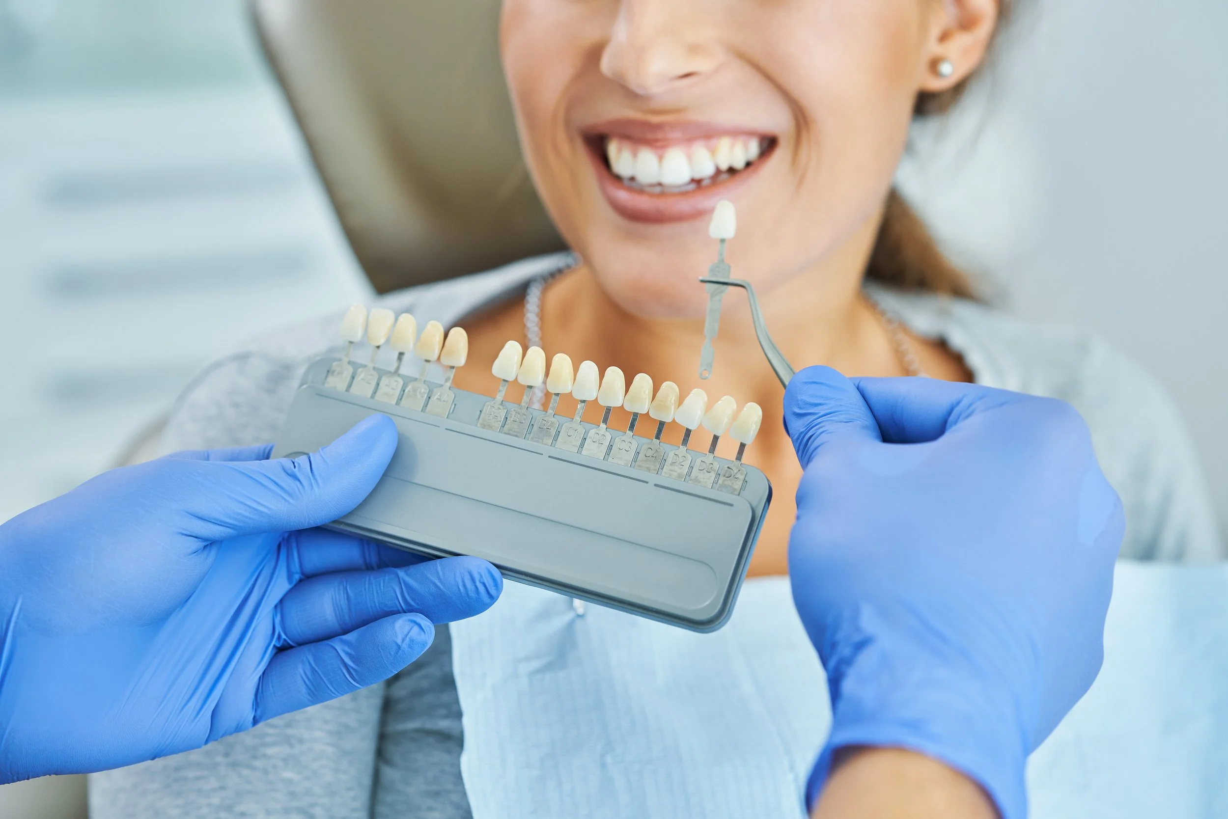 Dentist holding a shade guide next to a patient, smiling, for tooth color matching.