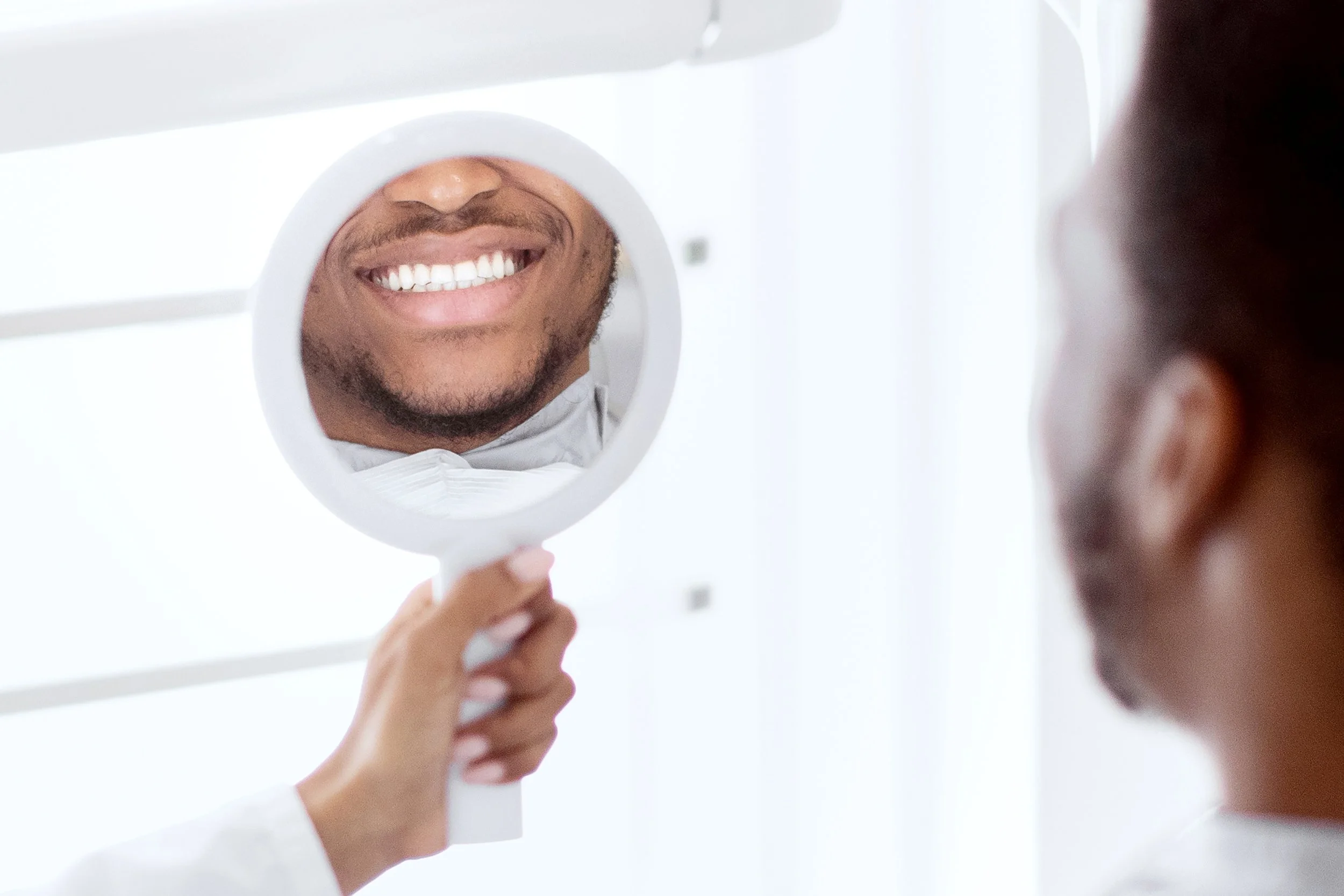 Person smiling while looking at reflection in small handheld mirror.