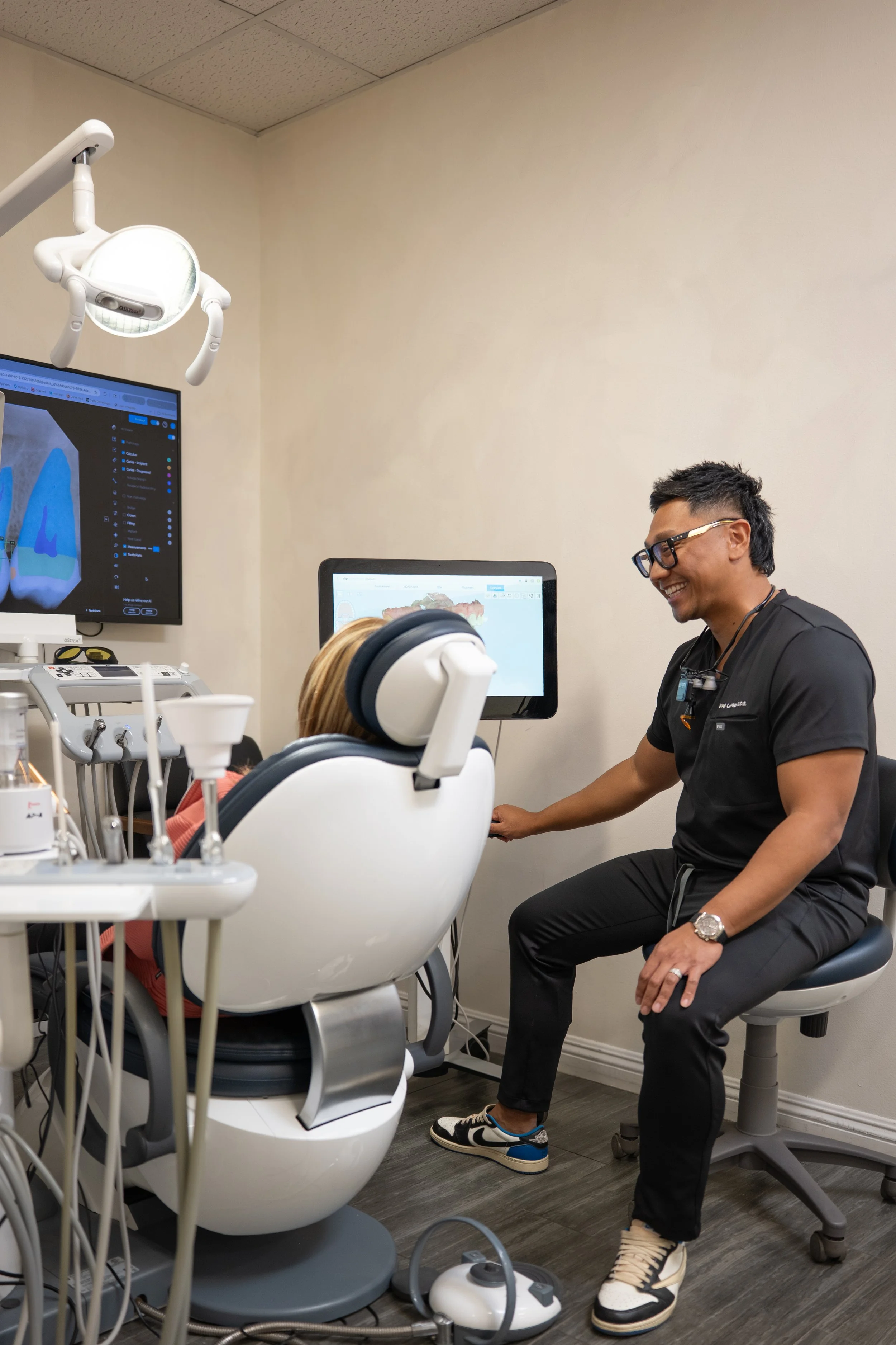 A dentist and a patient in a dental office, with dental equipment and screens displaying dental images.