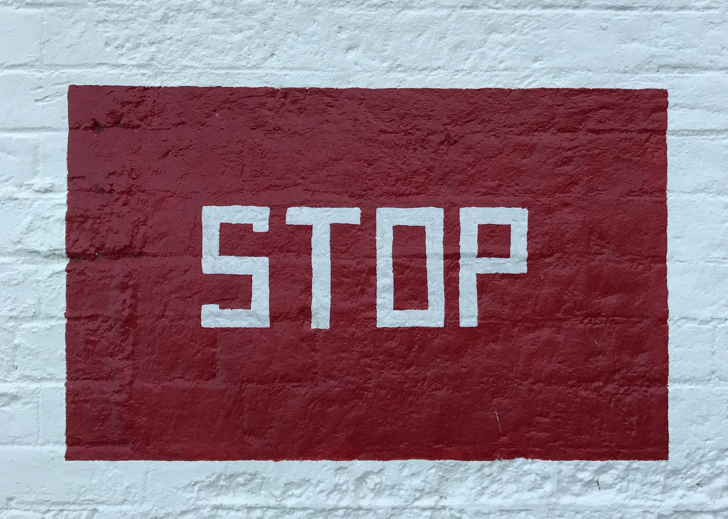 White “STOP” text on a red painted rectangle against a white painted brick wall.