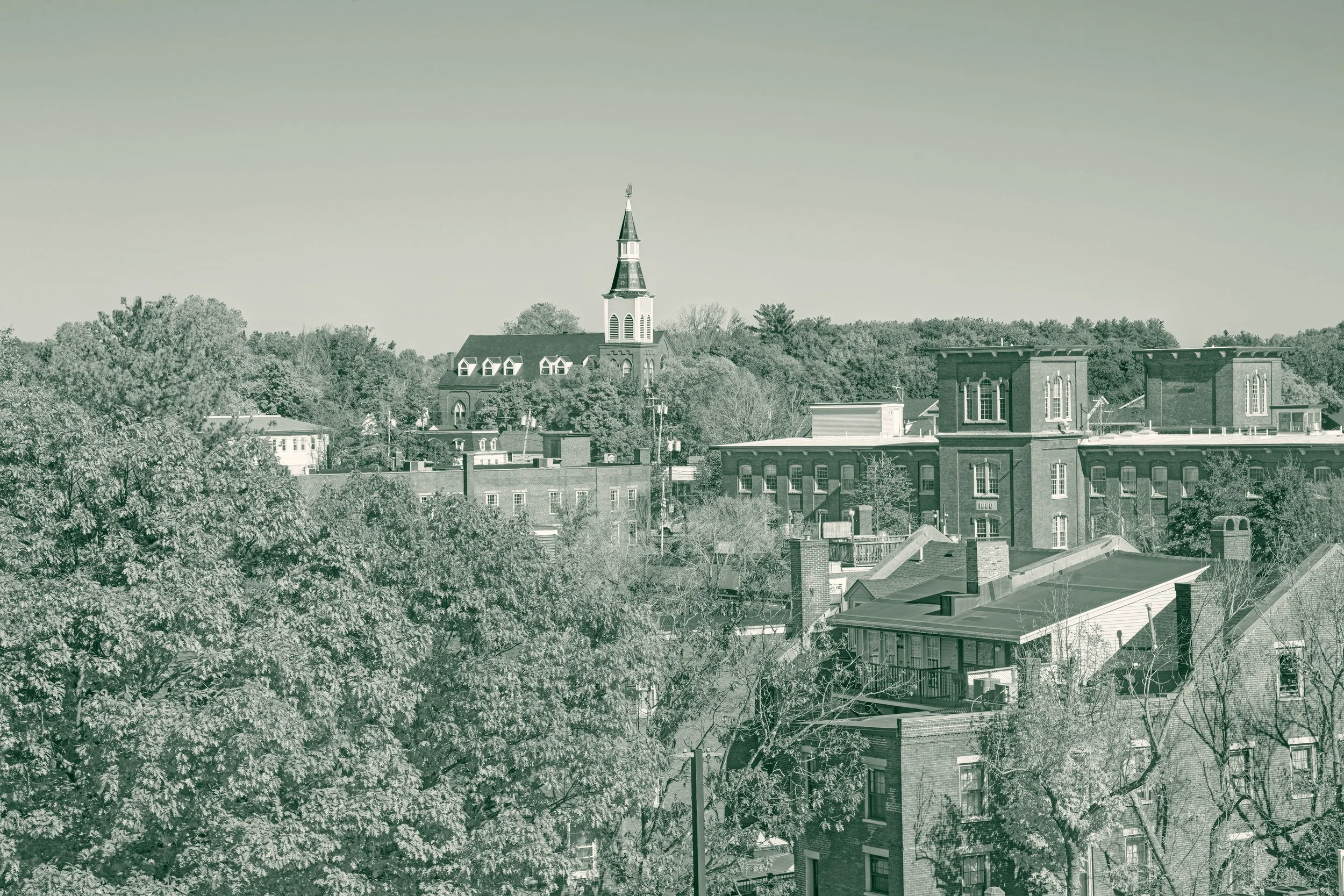 Autumn foliage over the rooftops of downtown Dover, New Hampshire, with a white church steeple and a brick mill block on the hillside behind
