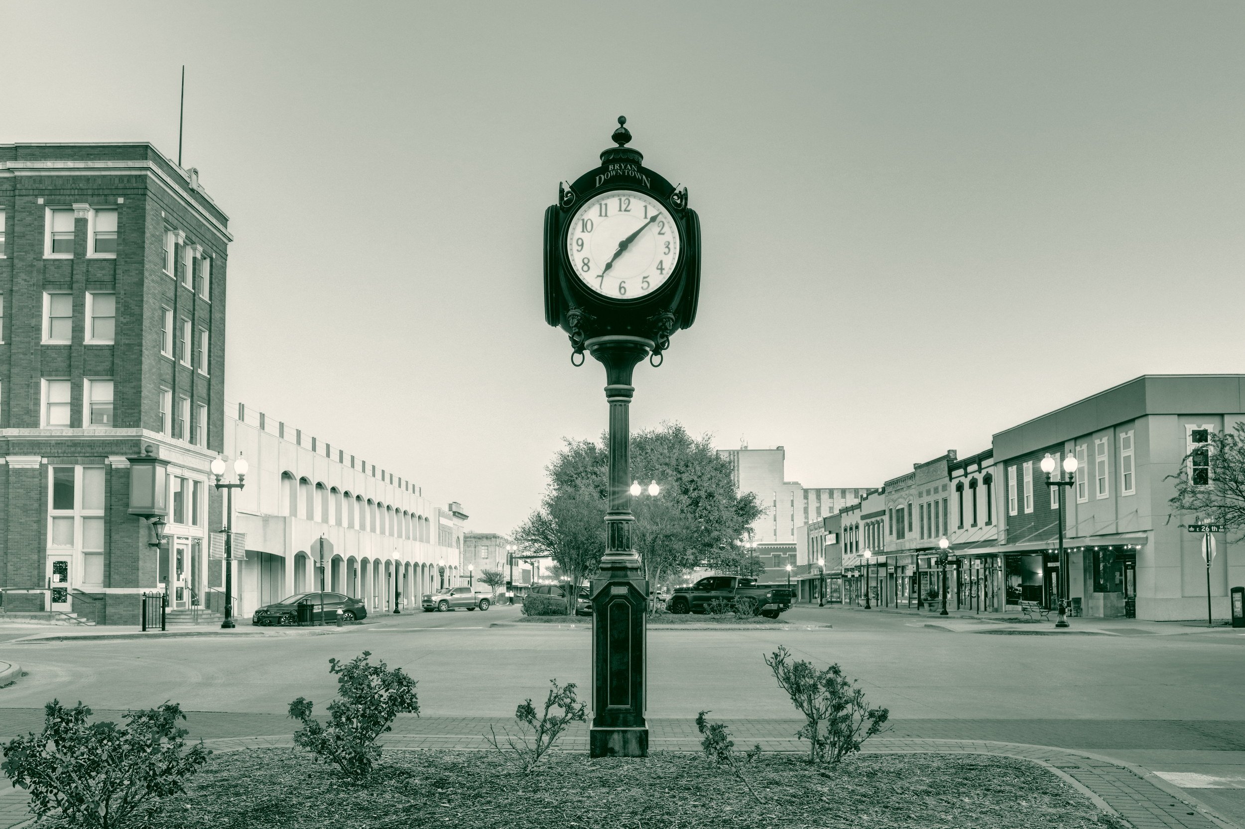 The clock tower in downtown Bryan, Texas, with historic brick storefronts lining the street behind it at dusk.