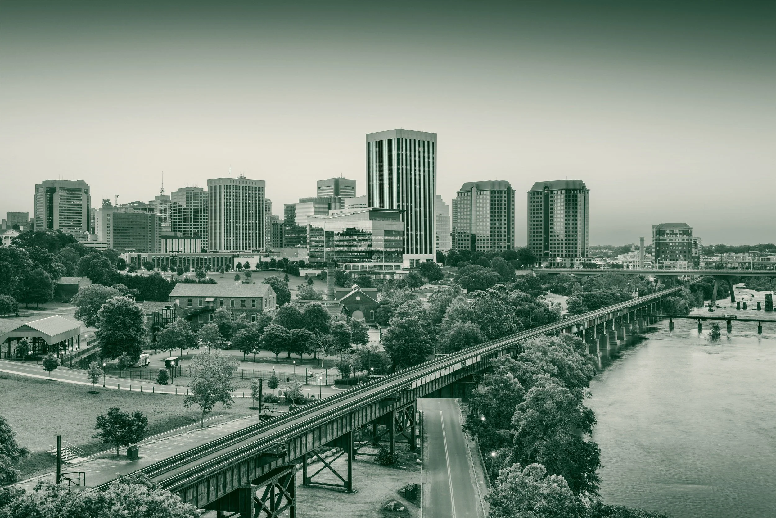 Downtown Richmond, Virginia skyline at dusk seen from across the James River, with a railroad trestle in the foreground