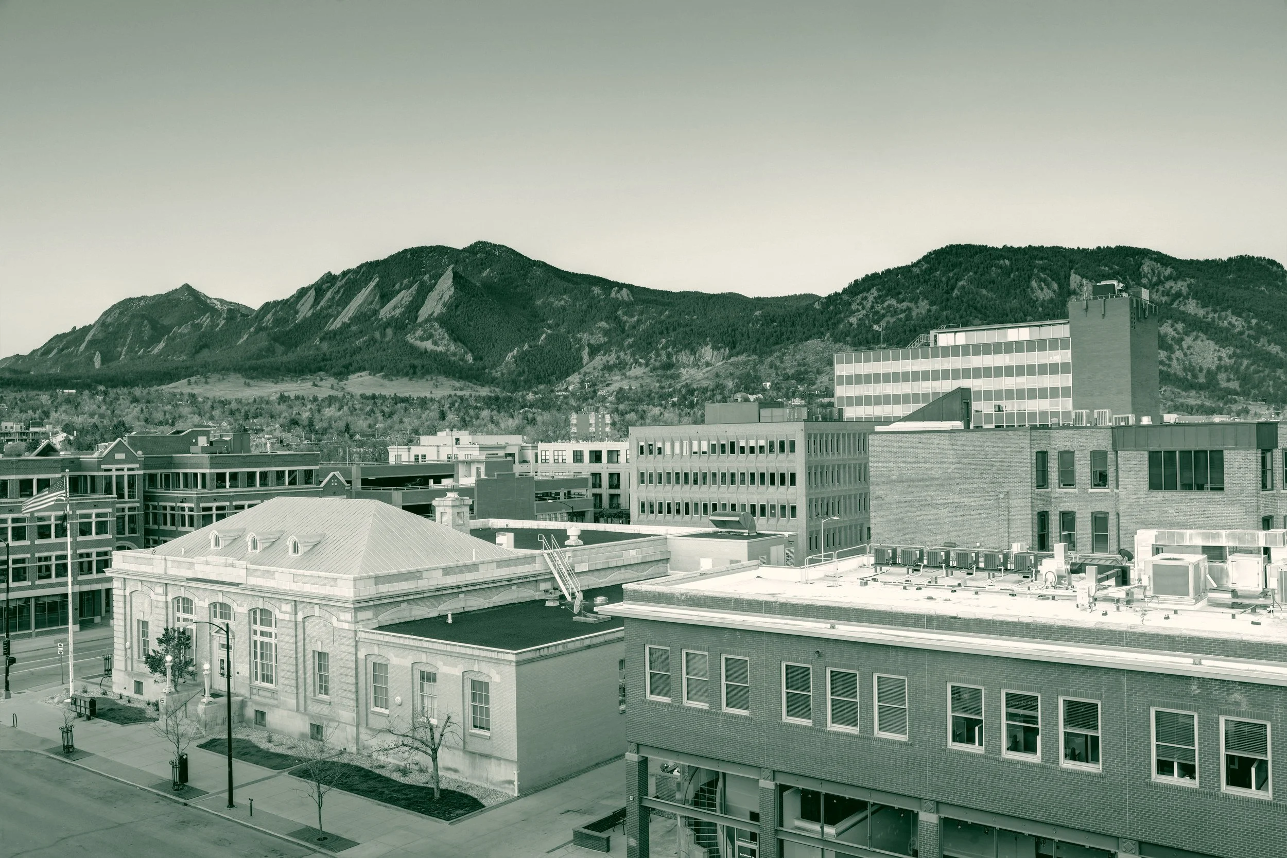 Downtown Boulder, Colorado at golden hour, with low brick and stone buildings in the foreground and the Flatirons rising behind the city.