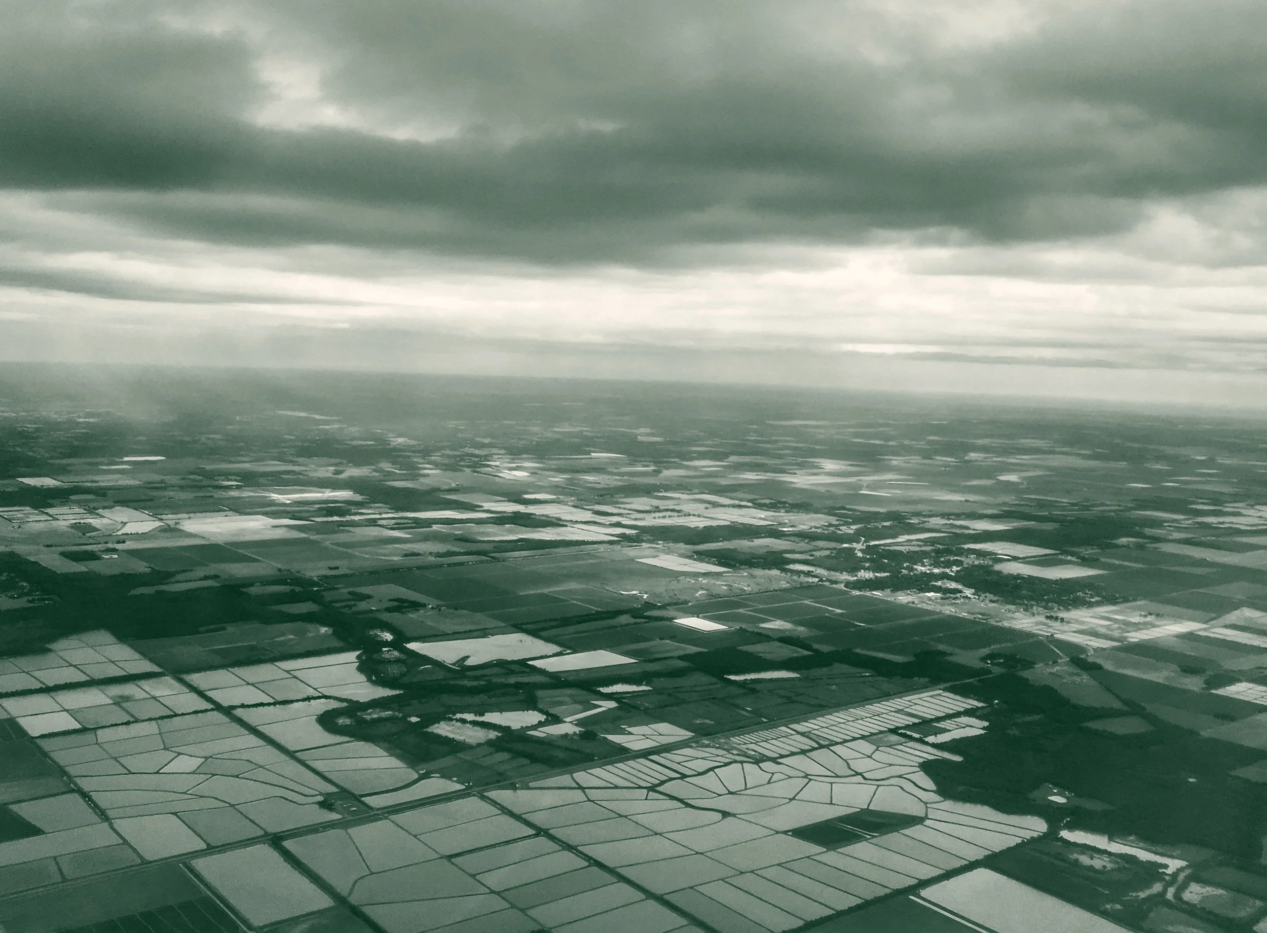 An aerial view of flooded rice fields and farm plots stretching to the horizon under a heavy, overcast sky in Arkansas.