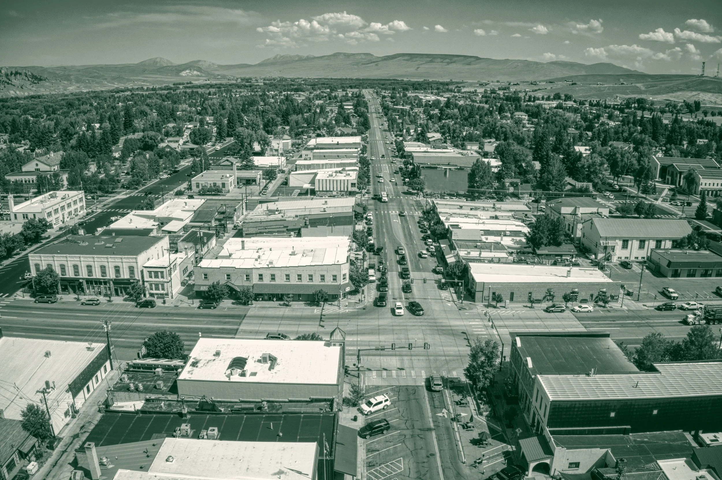 Aerial view down Main Street in Gunnison, Colorado, with brick storefronts on both sides and mountains beyond the valley.