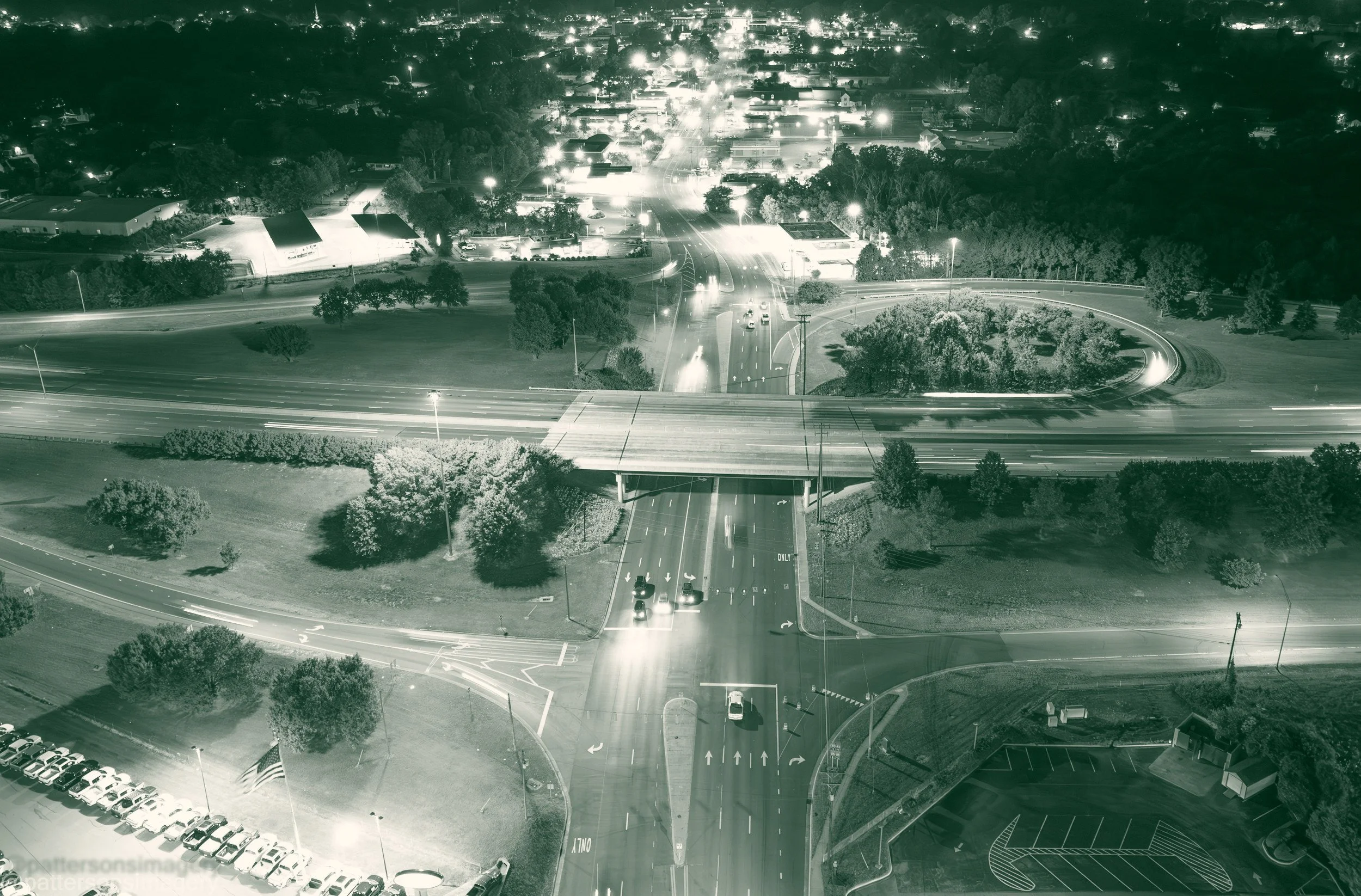 Aerial view at night of a highway interchange in Graham, North Carolina, with a lit road running under the overpass toward the town's businesses and neighborhoods, and light trails from traffic on the highway.