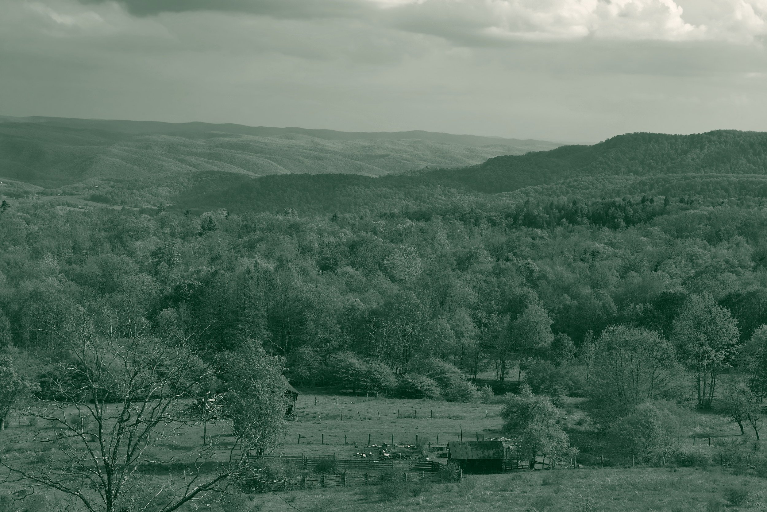A green valley in the West Virginia mountains, with a small barn and fenced pasture below layers of forested ridges.