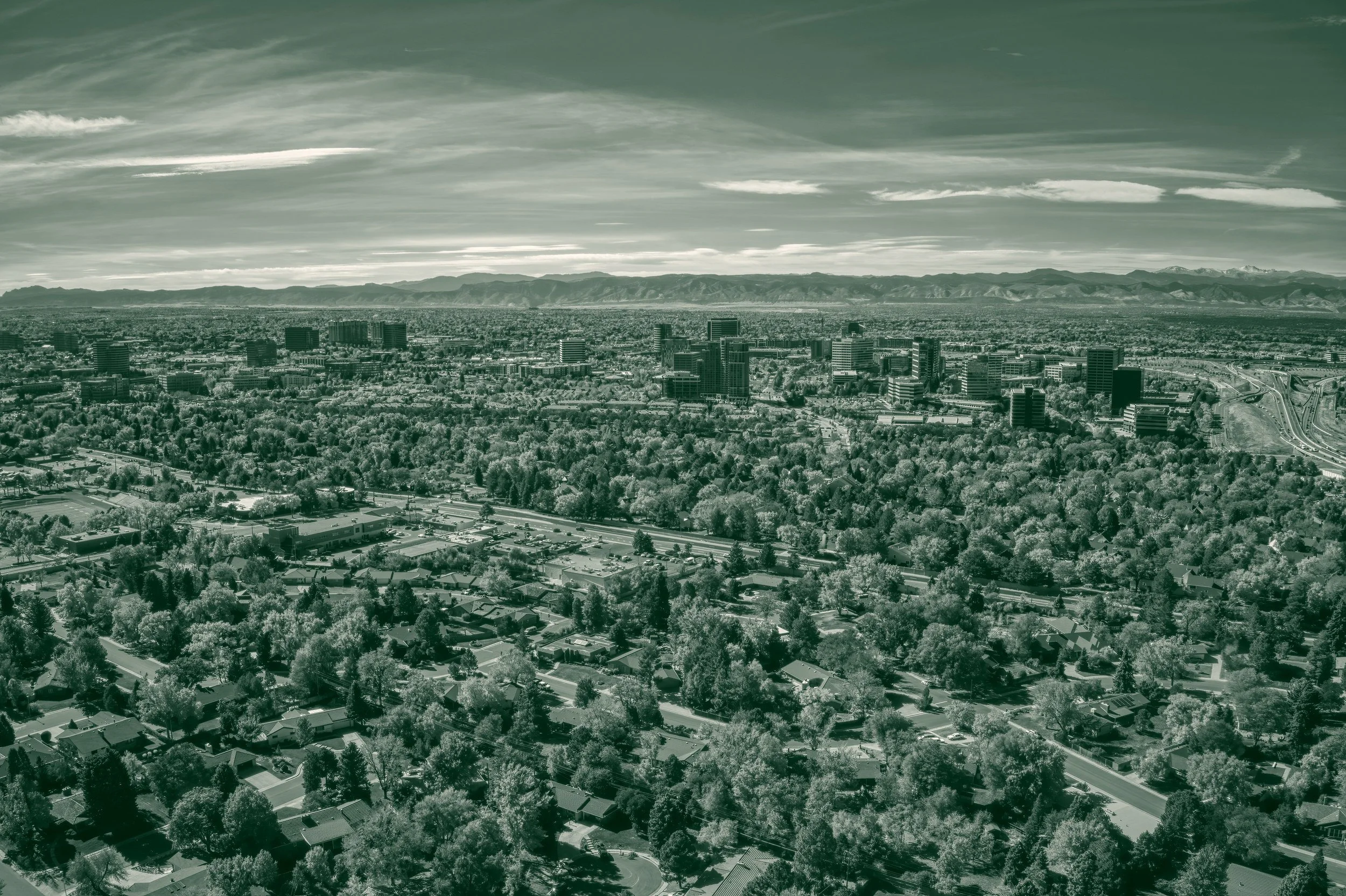 Aerial view of Aurora, Colorado, in autumn, with tree-lined neighborhoods in the foreground, office buildings in the middle distance and the Front Range on the horizon.
