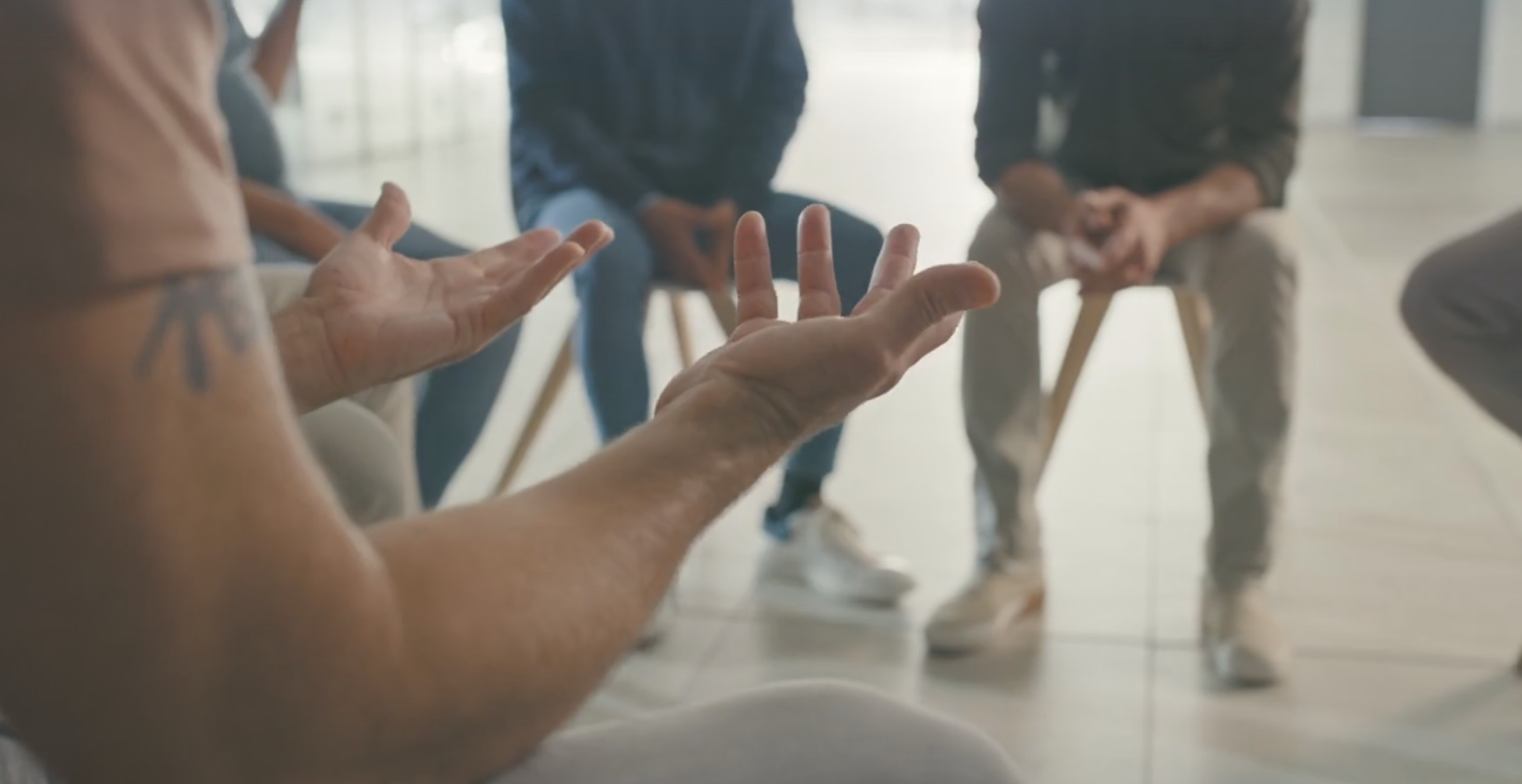 People seated in a circle, engaging in a discussion or therapy session in a bright room.