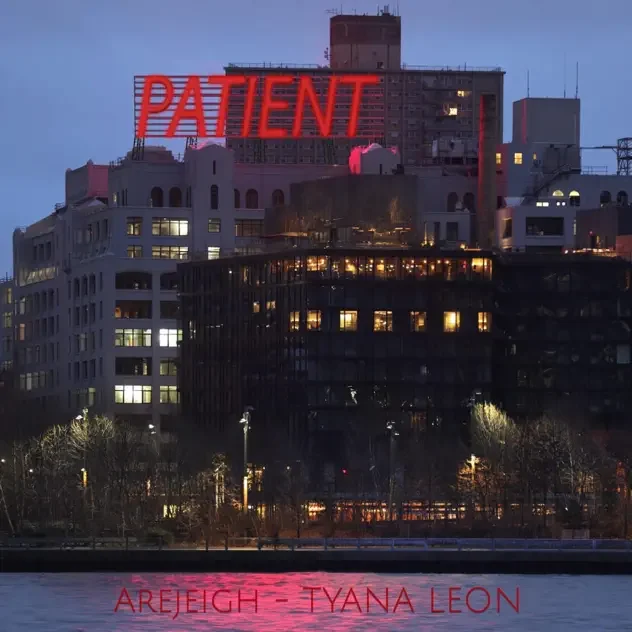 A cityscape at dusk with a building featuring a red neon sign that says PATIENT on the rooftop, and other buildings with lit windows, reflecting in a body of water.